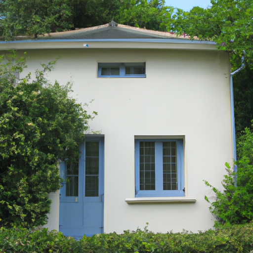 A light beige house with a dark blue door surrounded by lush green trees